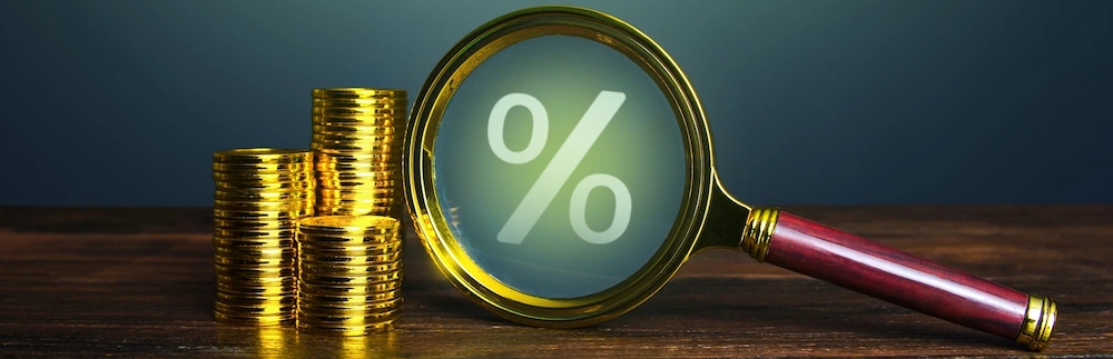 A golden magnifying glass is examining an illuminated percent symbol next to stacked gold coins representing efforts to maximize ROI on advertising investments.