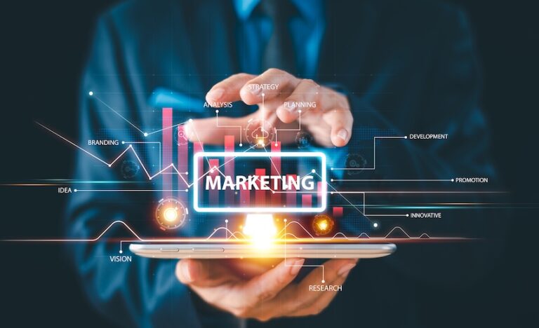A businessman in a suit holds a tablet as a glowing holographic display projects the word 'Marketing' surrounded by strategy-branding-planning-and research labels, visualizing the comprehensive services a modern marketing agency provides.