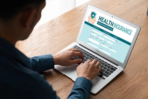 A man on his computer looking up health insurance represents healthcare website design services.